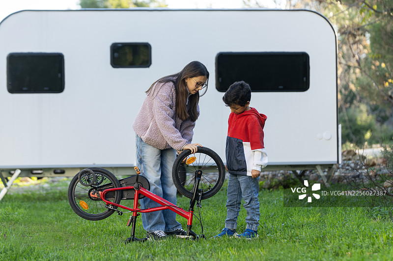 兄弟姐妹们在露营车附近一起修理自行车图片素材