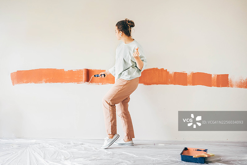 一位快乐的女士正在用充满活力的橙陶色粉刷白墙，同时翩翩起舞。图片素材