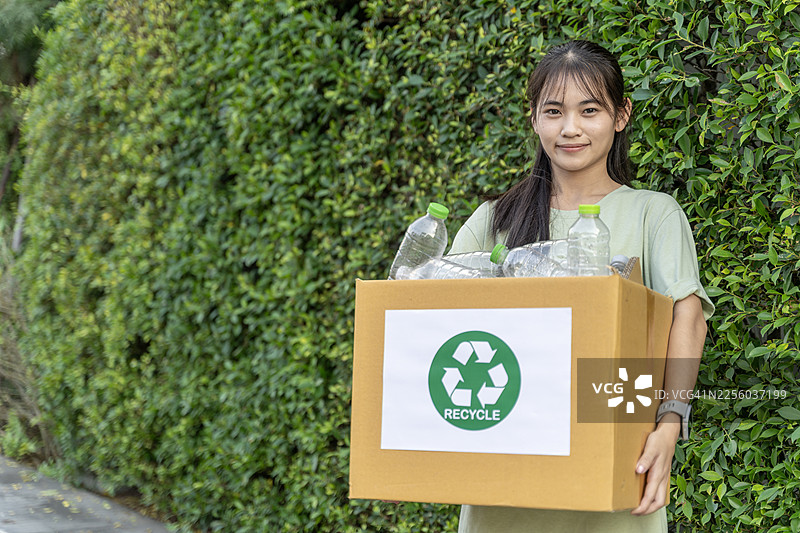 年轻女子手持回收箱，装有用于家庭垃圾分类的塑料瓶图片素材