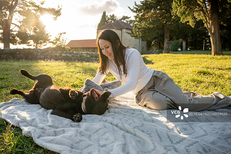 日落时分，女子在公园里抚摸一只快乐的巧克力拉布拉多犬图片素材