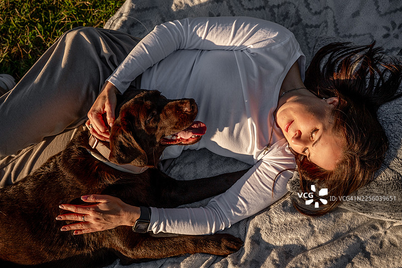 日落时分，女子与巧克力拉布拉多犬放松图片素材