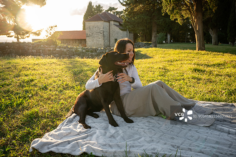 日落时分，女子在公园里拥抱她的巧克力拉布拉多犬图片素材
