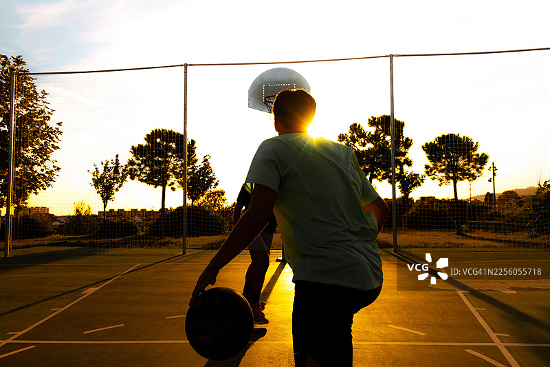 比赛中，一名年轻篮球运动员背对镜头，面对着黄昏的金光图片素材