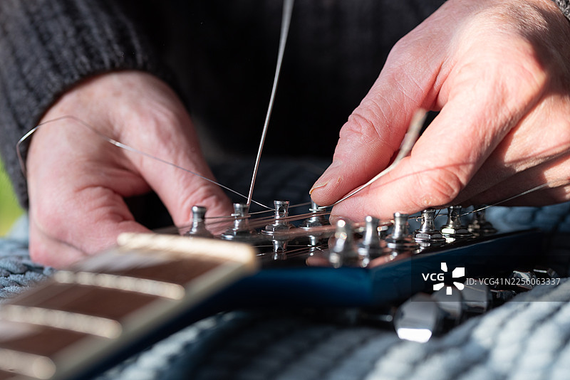 特写：在十二弦电吉他上装上新琴弦的双手图片素材