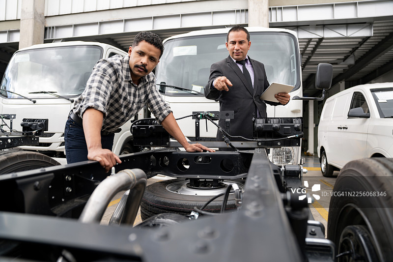 销售人员在向顾客推销时，用手指着卡车底盘图片素材