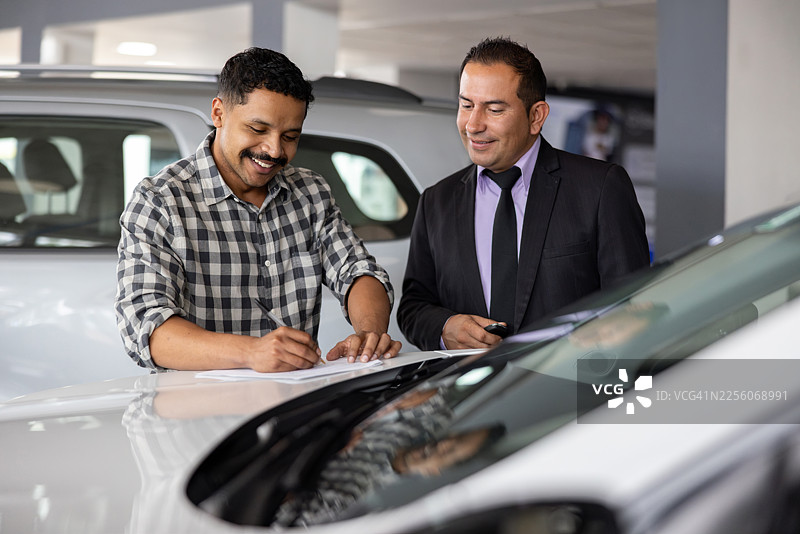 快乐的男人在经销商处签署他的汽车租赁协议图片素材