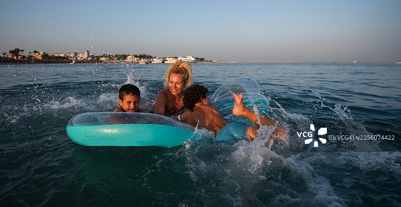 母亲和孩子们在日落时分的海边玩水嬉戏。图片素材