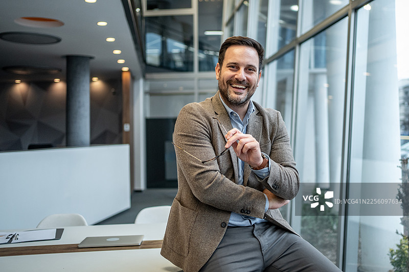 自信的商人在现代办公室里摆姿势微笑图片素材