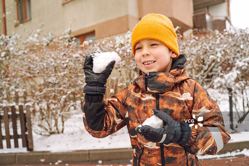 冬天，一个小男孩在院子里玩雪球图片素材