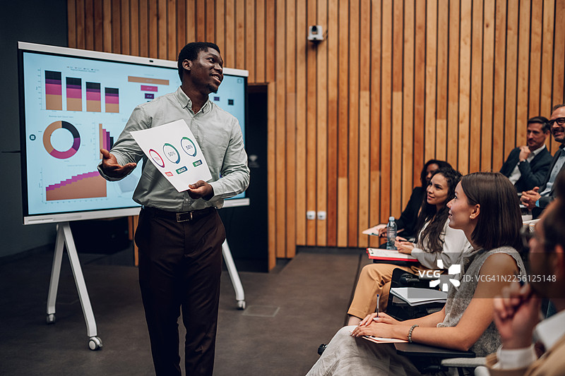 一位黑人商人在会议上向多元化观众展示数据图片素材
