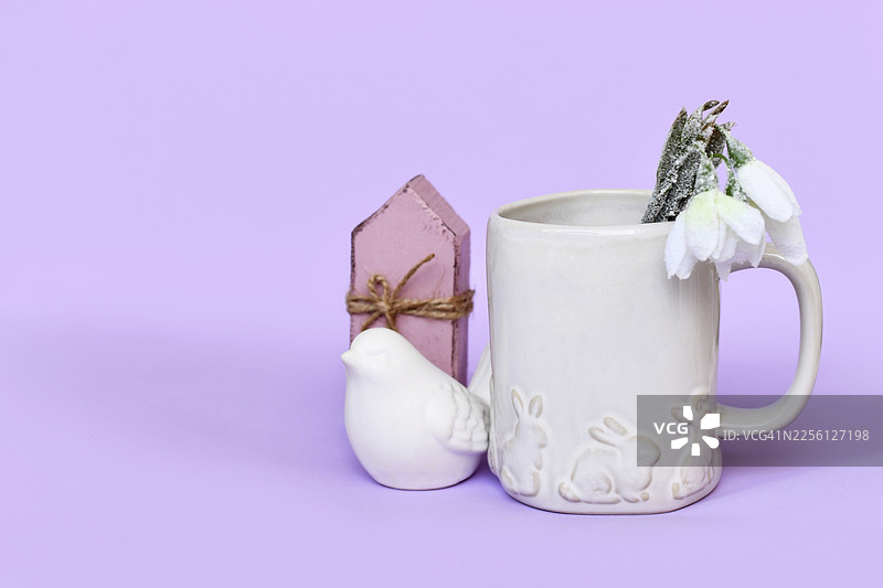 可爱春季装饰摆设，包含小鸟、郁金香花朵和兔子复活节主题马克杯，背景为紫色，带有复制空间图片素材