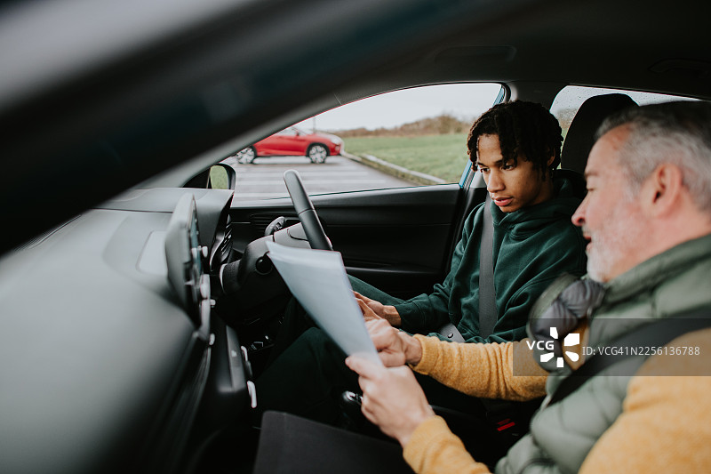 一名年轻男学生在右舵手动挡汽车上进行首次驾驶课程——教练在开始前会带他过一遍同意书和注意事项。图片素材