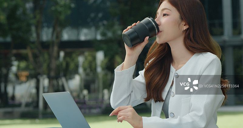 一位美丽的年轻亚洲女性在户外使用笔记本电脑和咖啡远程工作图片素材