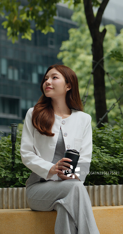 一位自信的年轻亚洲女性在户外手持平板电脑，抬头微笑图片素材