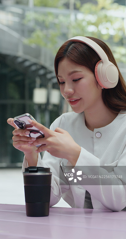 时尚的年轻亚洲女性在户外使用智能手机，佩戴无线耳机图片素材