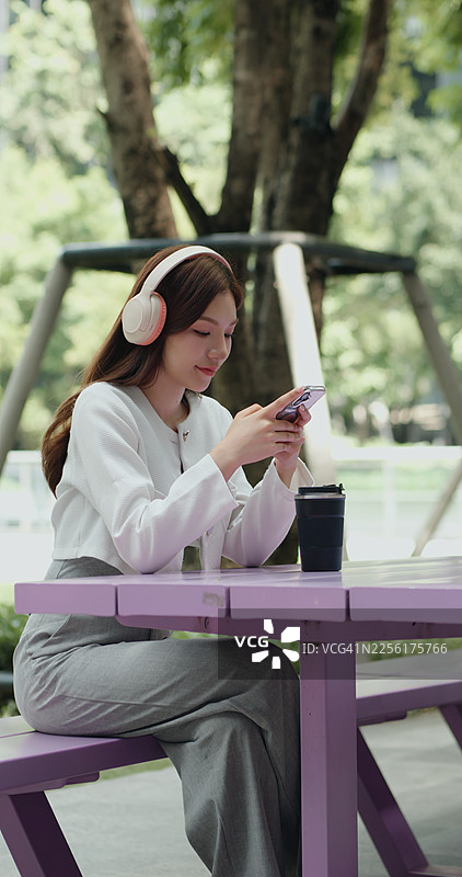 年轻时尚的亚洲女性户外使用智能手机并佩戴无线耳机图片素材