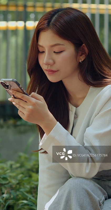 专注的年轻亚洲女性在户外使用智能手机图片素材