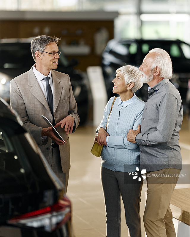 快乐的老年夫妇在展厅里与汽车销售员交谈。图片素材