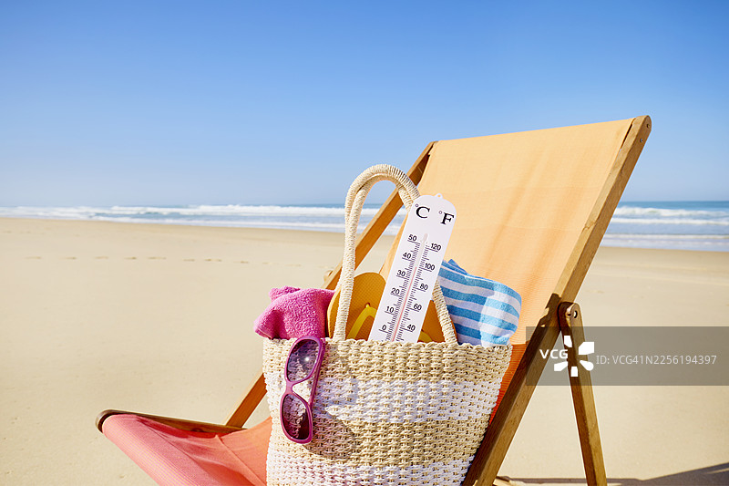 沙滩椅上的沙滩包里的温度计，背景是海与蓝天图片素材