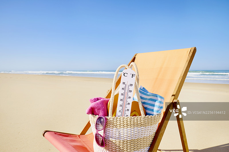 沙滩椅上的沙滩包里的温度计，背景是海洋和蓝天图片素材