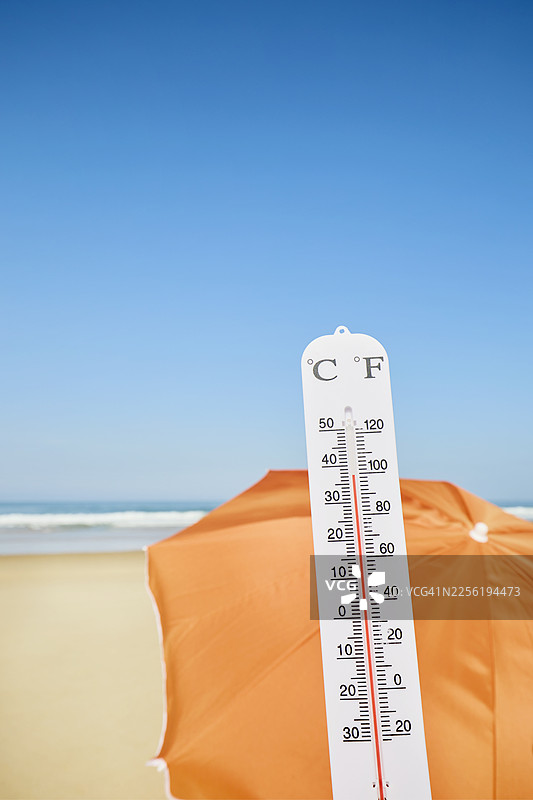 阳光明媚的一天，海滩和大海旁的橘色遮阳伞下放着温度计图片素材