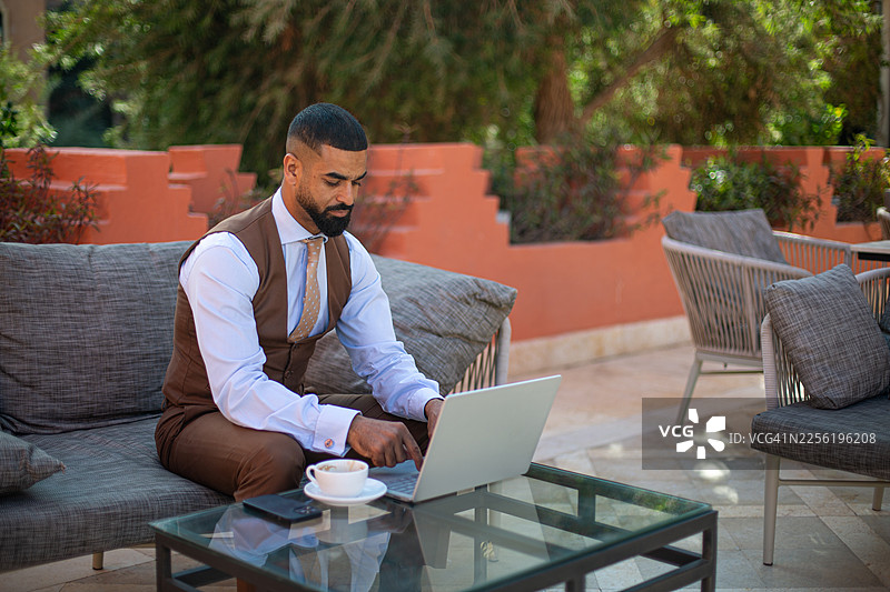 年轻男子在户外咖啡馆使用笔记本电脑工作图片素材
