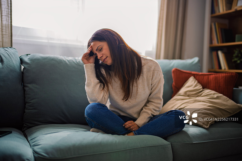 年轻女子在家中坐在沙发上，痛苦地捂着头图片素材