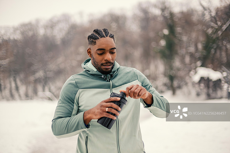 年轻黑人男性在冬季的户外雪地里准备蛋白粉饮料图片素材