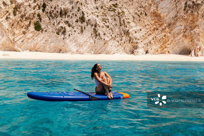 一名身穿白色泳衣的女子躺在桨板上图片素材
