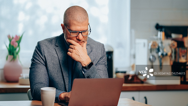 中年商人居家办公室使用笔记本电脑工作，旁边放着咖啡图片素材