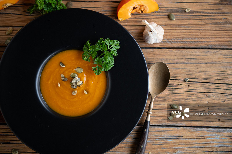 质朴的木桌上，黑碗盛着南瓜汤图片素材