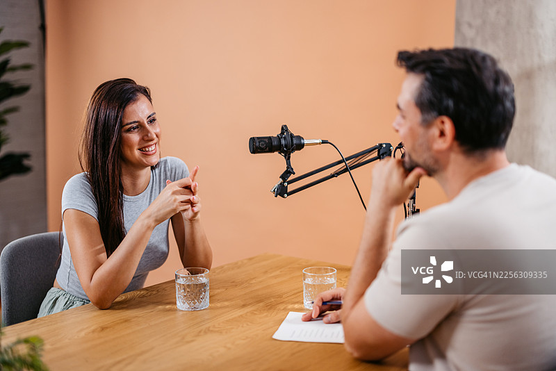 播音室里，一位男主持人与一位女嘉宾正在对着麦克风交谈图片素材