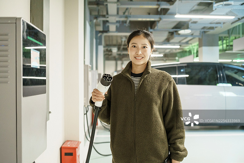 亚洲女性在地下车库使用电动汽车充电桩、新能源汽车、移动支付和电动汽车图片素材