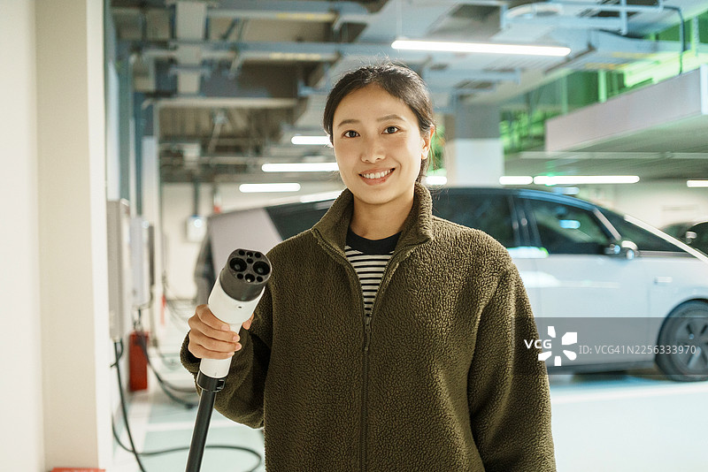 亚洲女性在地下车库使用电动汽车充电桩、新能源汽车、移动支付和电动汽车图片素材