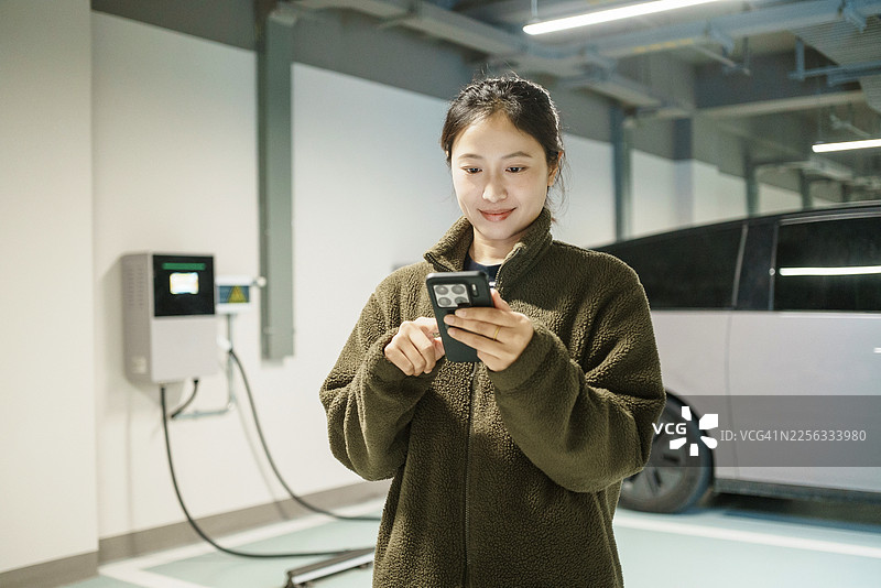 亚洲女性在地下车库使用电动汽车充电桩、新能源汽车、移动支付和电动汽车图片素材