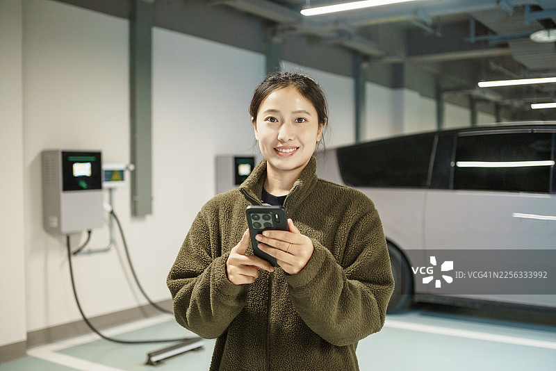 亚洲女性在地下车库使用电动汽车充电桩、新能源汽车、移动支付和电动汽车图片素材