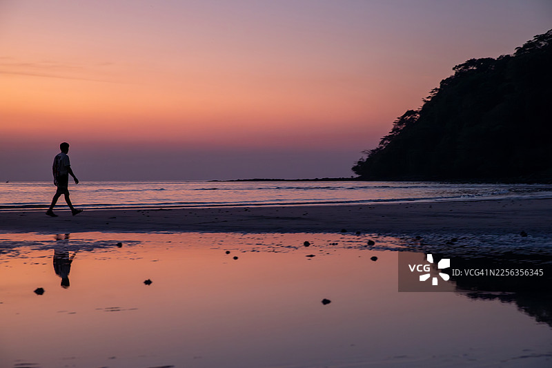 戈公岛 - 暮色中，一名男子独自走在戈公岛海岸线上的剪影。美丽的日落天空和宁静水面的倒影。图片素材