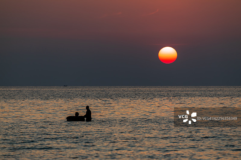 戈公岛 - 游客在戈公岛海滩附近的海中，利用充气圈（游泳圈）玩水的剪影，正值日落时分。图片素材