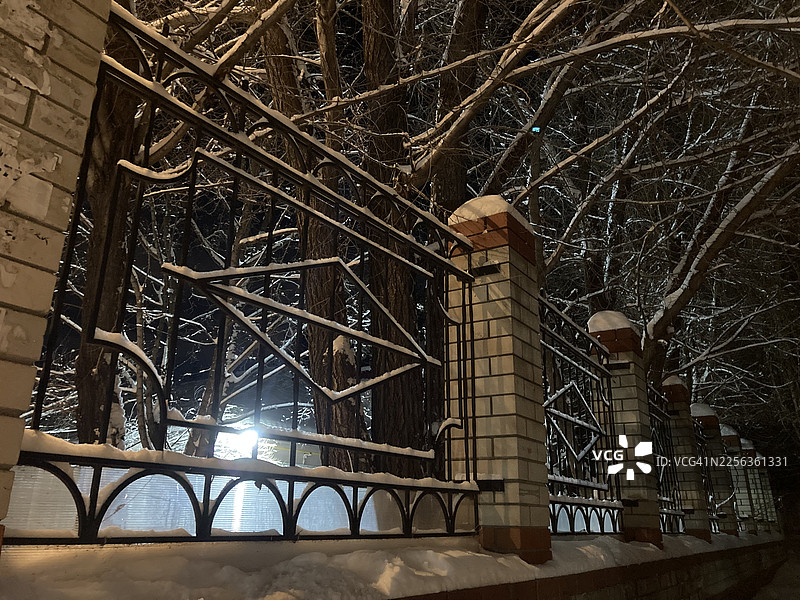 雪夜，沿着绿树成荫的小路，砖柱和结霜的铁栏杆组成的栅栏图片素材