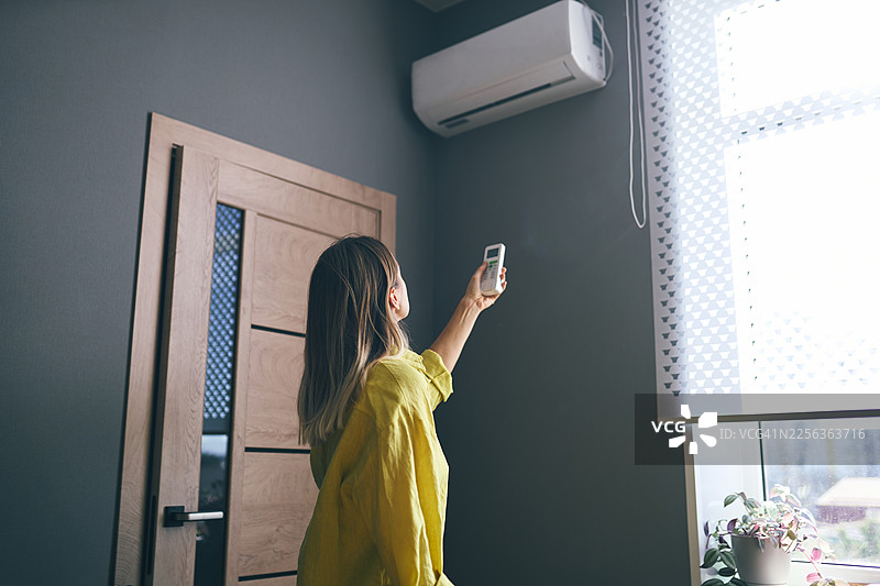 女人在家用遥控器调节空调图片素材