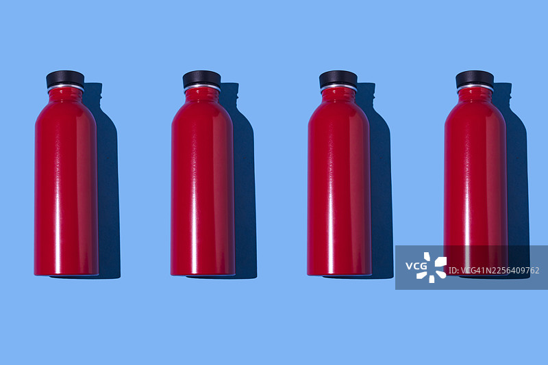 蓝色背景上的一排红色金属保温瓶图案。水、液体、可销售、可持续、可回收、明亮简约。图片素材