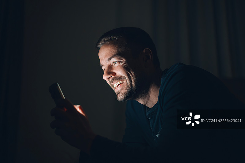 夜间，一名男子对着手机微笑，接收好消息图片素材