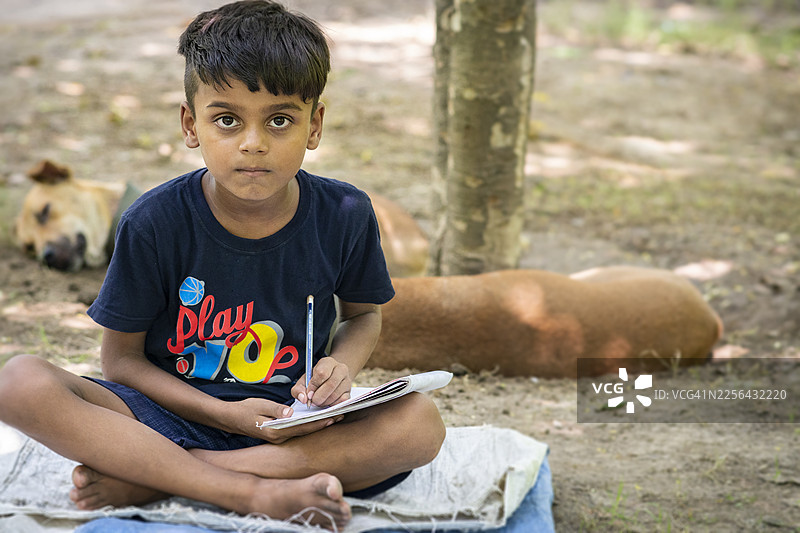 一名印度乡村晚期青少年男孩的户外肖像，他正在笔记本上写笔记并做家庭作业。图片素材