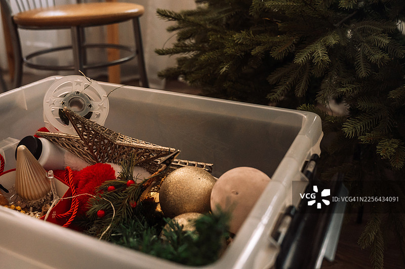装有圣诞装饰品的塑料收纳盒，旁边是装饰好的圣诞树，节日清理概念图片素材