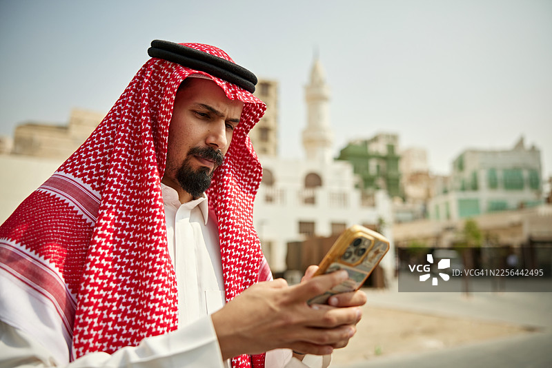 一名中年沙特男子在吉达老城区使用智能手机图片素材