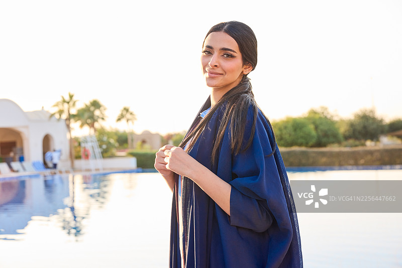 一位身着阿巴亚的美丽阿拉伯女子站在豪华度假村的泳池旁图片素材