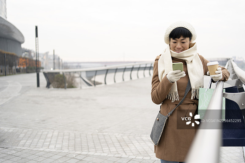 冬天，一位亚洲女性一边喝着咖啡，一边在网上购物图片素材