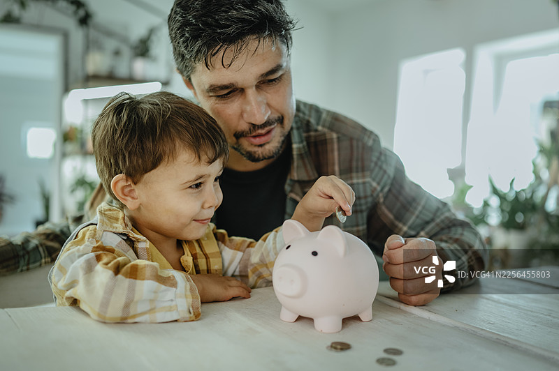 父亲和儿子在家往储蓄罐里投币图片素材