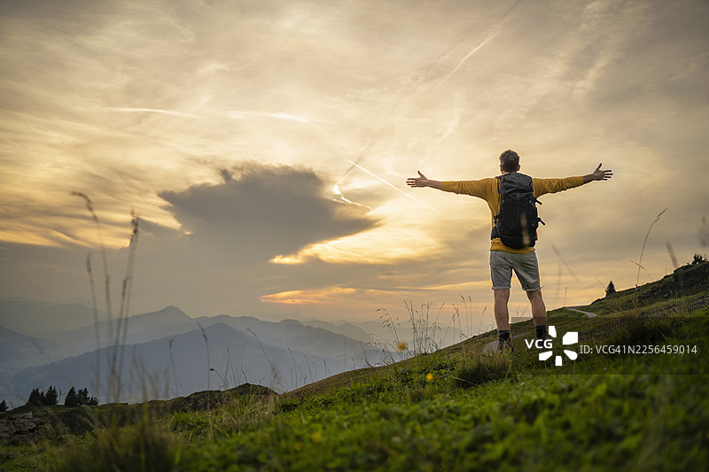 日出时分，一个无忧无虑的徒步者张开双臂站在山顶上图片素材