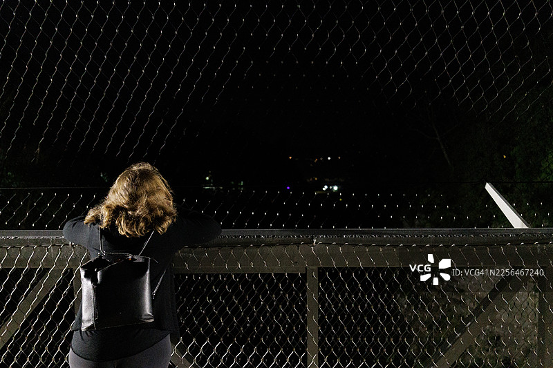 夜间，一名女子在纽约伊萨卡，透过桥梁安保围栏向外望去图片素材